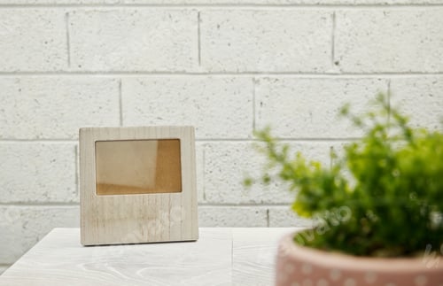 Preview: Concept shot of blank wooden photo frame on wooden desk with house plant and brick wall background