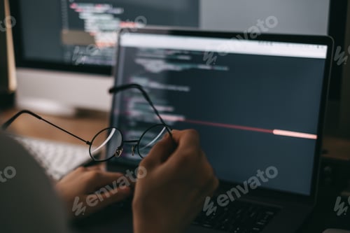 Preview: Young caucasian female programmer in glasses writes program code on a laptop computer. home office