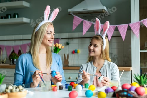 Preview: Mom with daughter in bunny ears paint Easter eggs in the kitchen.
