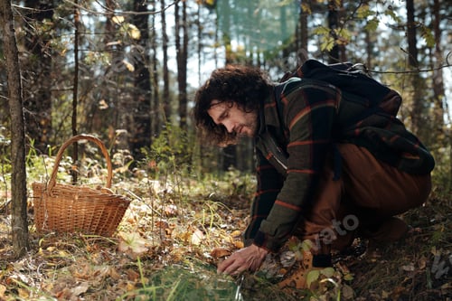 Preview: Side view of young male backpacker cutting fresh boletus with knife