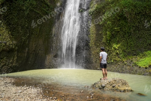 Preview: young asian indonesian man standing against the waterfall