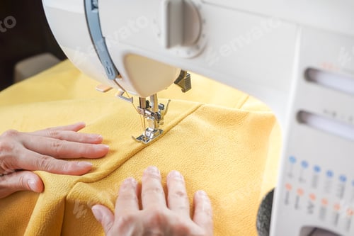 Preview: Tailor Hands Stitching Yellow Fabric On Modern Sewing Machine At Workplace In Atelier