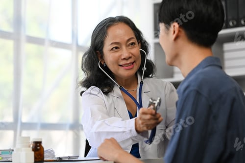 Preview: Positive mature doctor using stethoscope, listening to male patient breath or heartbeat.