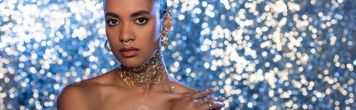 Preview: African american woman with golden foil on neck touching naked shoulder on sparkling background,