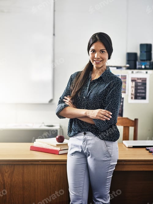 Visualização: Retrato de uma atraente jovem professora de pé com os braços cruzados em uma sala de aula