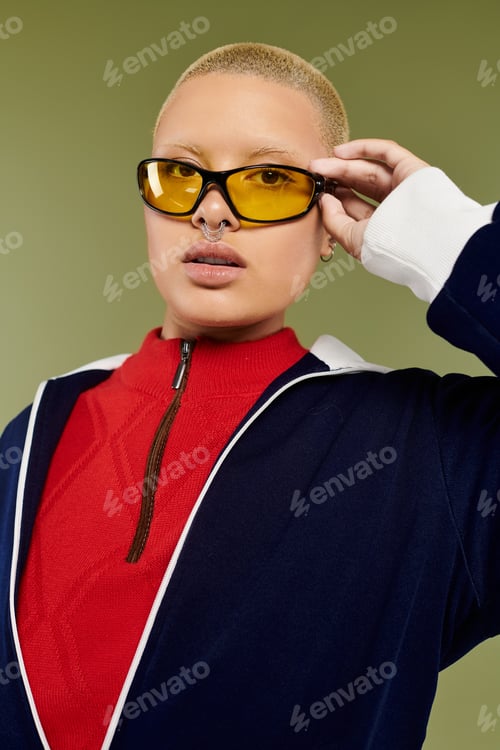 Preview: A trendy young bald woman in vibrant attire poses confidently against a green backdrop
