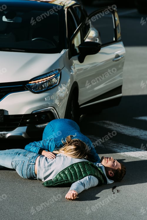 Preview: high angle view of woman checking heartbeat of injured man lying on road after car accident