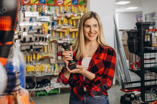 Preview: Beautiful smiling saleswoman is selling a drill at hardware store.