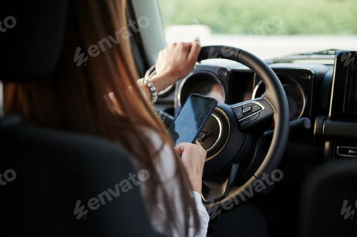 Preview: Using smartphone. Particle view of woman that drives modern new car in the city
