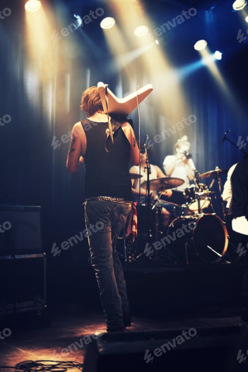 Preview: Rocking out. A guitarist on stage with his band beneath strobe lights in a nightclub.
