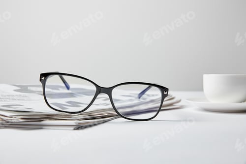 Preview: selective focus of glasses near business newspaper and cup on white