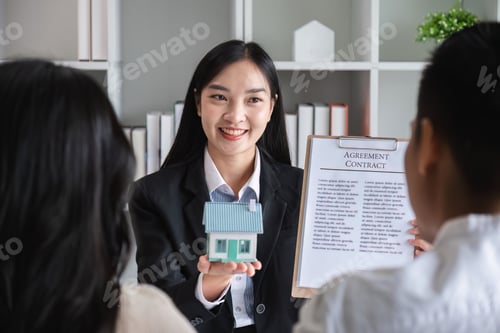 Preview: Happy Couple Signing Real Estate Sales Contract with Agent Holding Model House in Modern Office