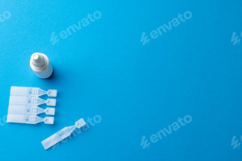 Preview: Overhead of saline solution caplets and dropper bottle on blue background with copy space