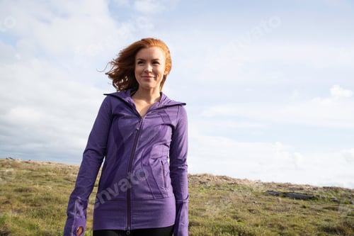 Preview: Redhead woman outside in countryside wearing purple workout jacket