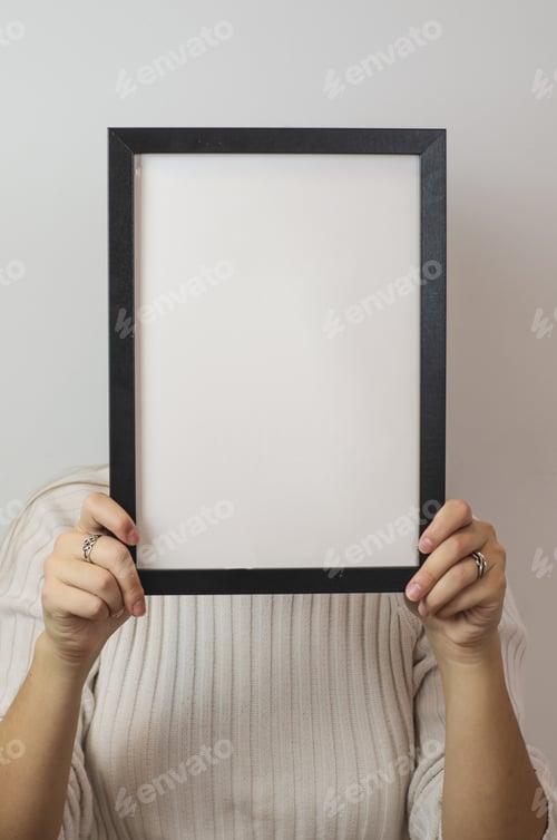 Preview: Vertical shot of a woman holding a plain white blank sign paper with a black frame covering her face