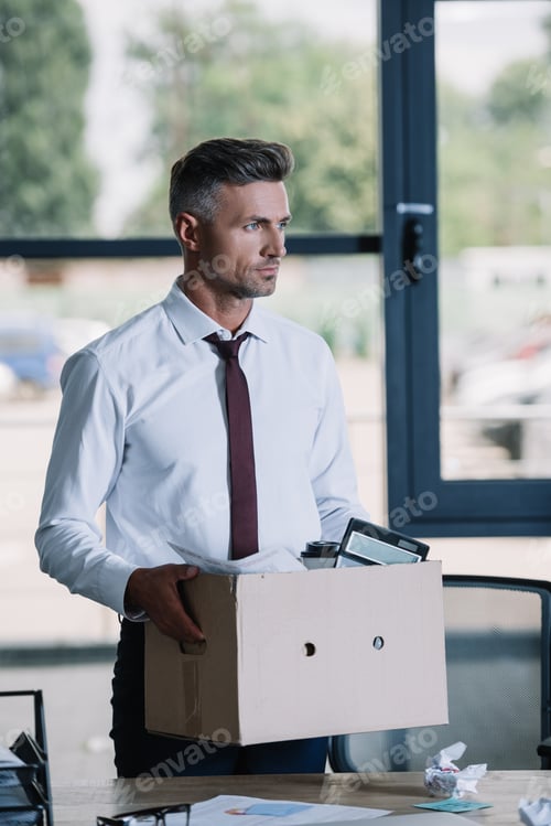 Preview: handsome businessman in suit holding box near workplace