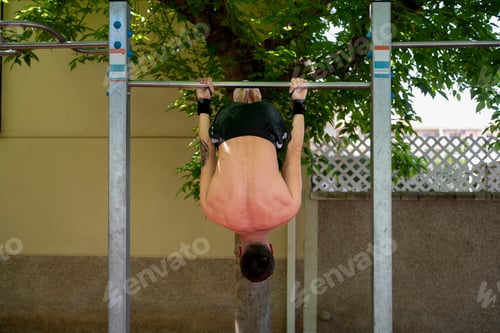 Preview: Determined athlete performing hanging leg raises on outdoor gym bar