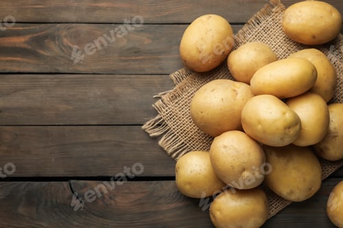 Preview: Many raw potatoes and burlap fabric on wooden table, flat lay. Space for text