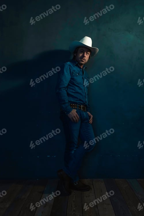 Preview: Man Wearing Denim Shirt And Cowboy Hat Standing Against Wall.
