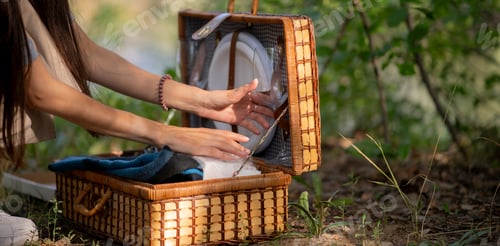Preview: a man squats down while carefully tending to a small grill set up in a grassy area near a forest lak