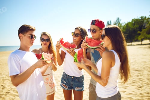 Preview: Group of friends having fun eating watermelon on beach. Excellent sunny weather. Super mood. Summer