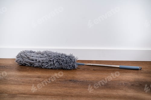 Preview: Grey duster tool on wooden floor near white wall. Housekeeping chores. Home hygiene