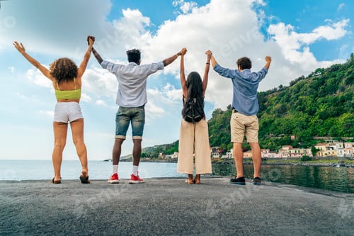 Preview: Back view of a group of diverse friends holding hands with arms raised celebrating.