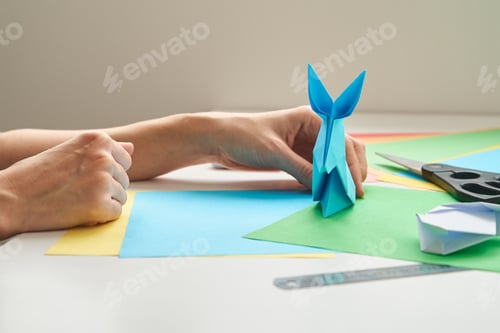 Preview: DIY concept. Woman make origami easter rabbit from color paper. Origami lessons