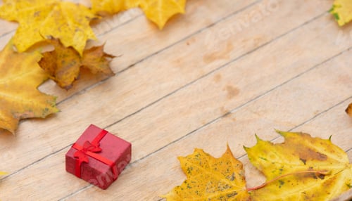 Preview: Little red gift box and maple leaves around on wooden table