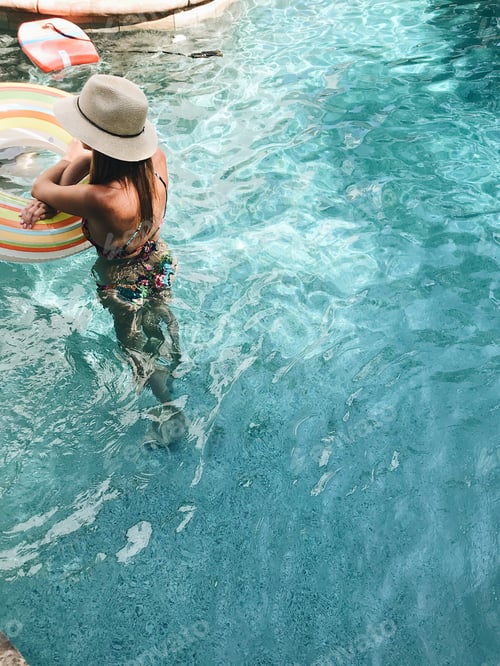 Preview: Young lady standing in a pool and leaning on a floating doughnut
