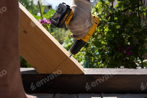 Preview: A carpenter works with a yellow electric screwdriver, twists a screw into a wooden plank beam