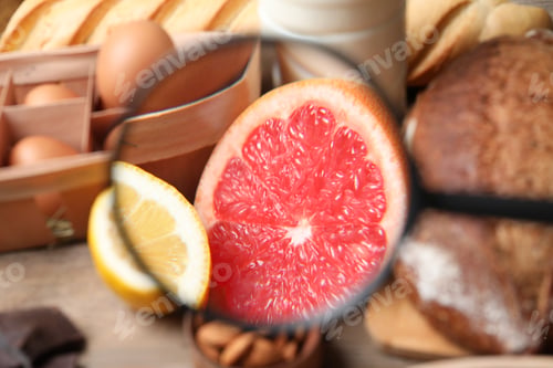Preview: Different products with magnifier focused on grapefruit and lemon, closeup. Food allergy concept