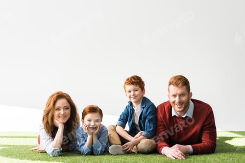 Preview: beautiful happy redhead family lying on grass and smiling at camera on grey