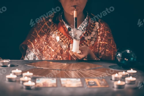 Preview: Tarot reader with tarot cards.Tarot cards face down on table near burning candles and crystal ball.