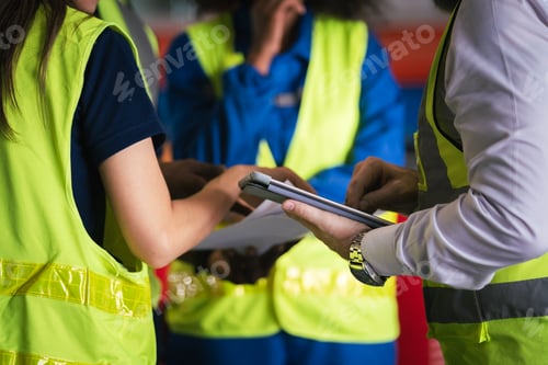 Preview: Group of diverse factory workers in safety uniform discussing job task in warehouse