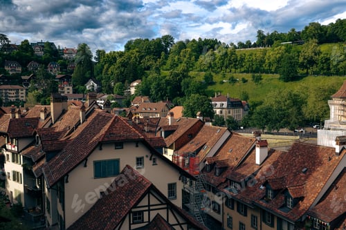 Preview: Scenic view of Bern\'s charming rooftops and lush hillside in Switzerland under a dynamic sky
