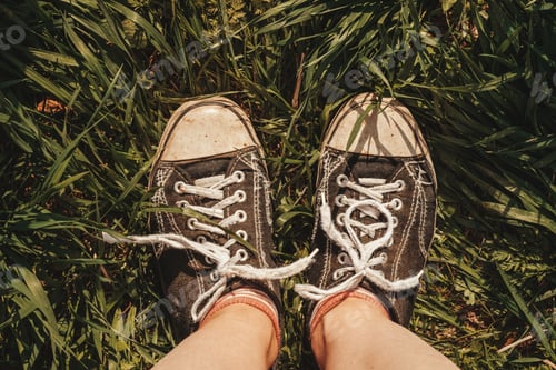 Preview: Close-up of feet in old sneakers on the grass on a summer day.