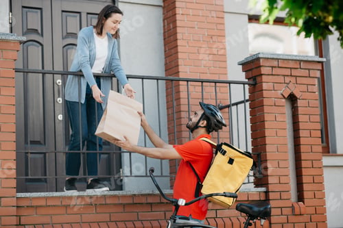 Preview: Customer, delivery and courier. Girl takes bag from man with backpack and bicycle, near front door