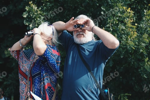 Preview: elderly couple. Senior couple. a man and a woman look through binoculars in different directions