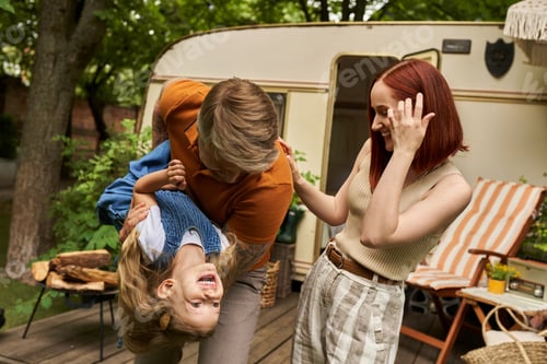 Preview: man playing with laughing daughter near happy wife and mobile home in trailer park, quality time