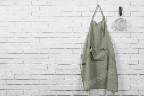 Preview: Clean kitchen apron with pattern and sieve on white brick wall. Space for text