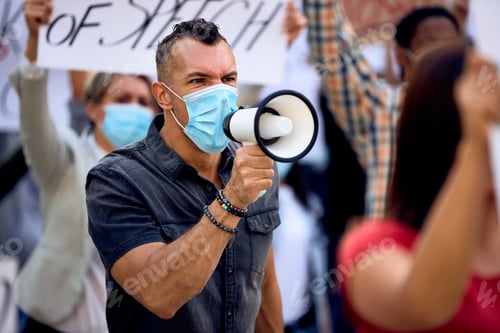 Preview: Caucasian man wearing face mask while shouting through megaphone on anti-lockdown protest.