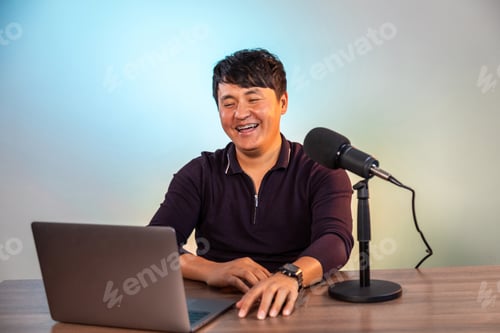 Preview: Smiling asian man looking at the laptop in a studio with microphone