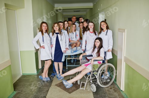 Preview: Crazy young doctors having fun by posing on a wheelchair in the hallway of hospital.