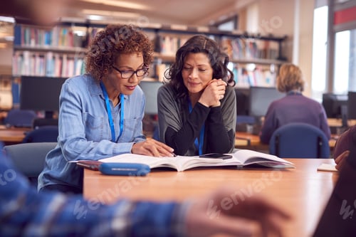 Preview: Teacher With Mature Female Adult Student Sitting At Table Working In College Library