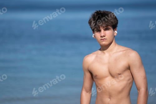 Preview: Young confident man wearing earbuds posing isolated on blue sea water in summer