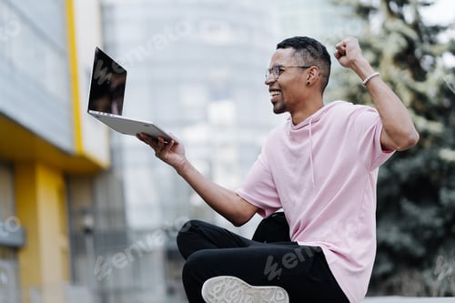 Preview: Fortunate man sit outdoors with laptop on building background