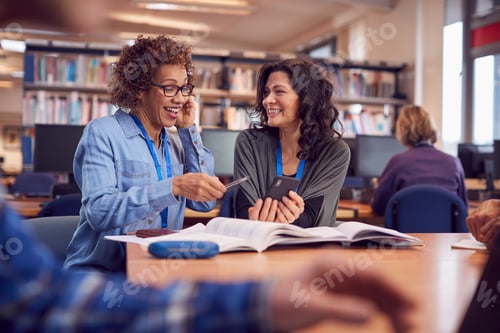 Preview: Teacher With Mature Female Adult Student Using Mobile Phone At Table Working In College Library