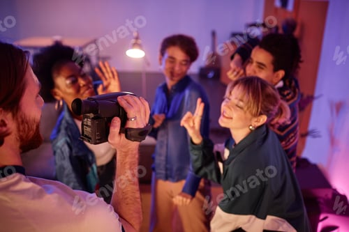 Visualização: Homem segurando uma câmera de vídeo retrô e filmando um vídeo caseiro de amigos se divertindo