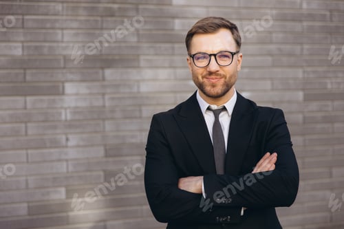 Preview: Confident businessman smiling with arms crossed in front of gray wall